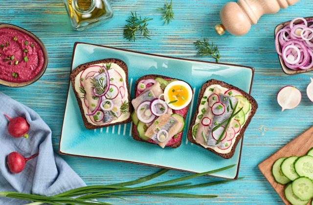 Smorrebrod traditional Danish sandwiches fish, radish, mayonnaise. Open sandwich with rye bread, herring on blue wooden background, top view. Tasty fish smorrebrod. Flat lay